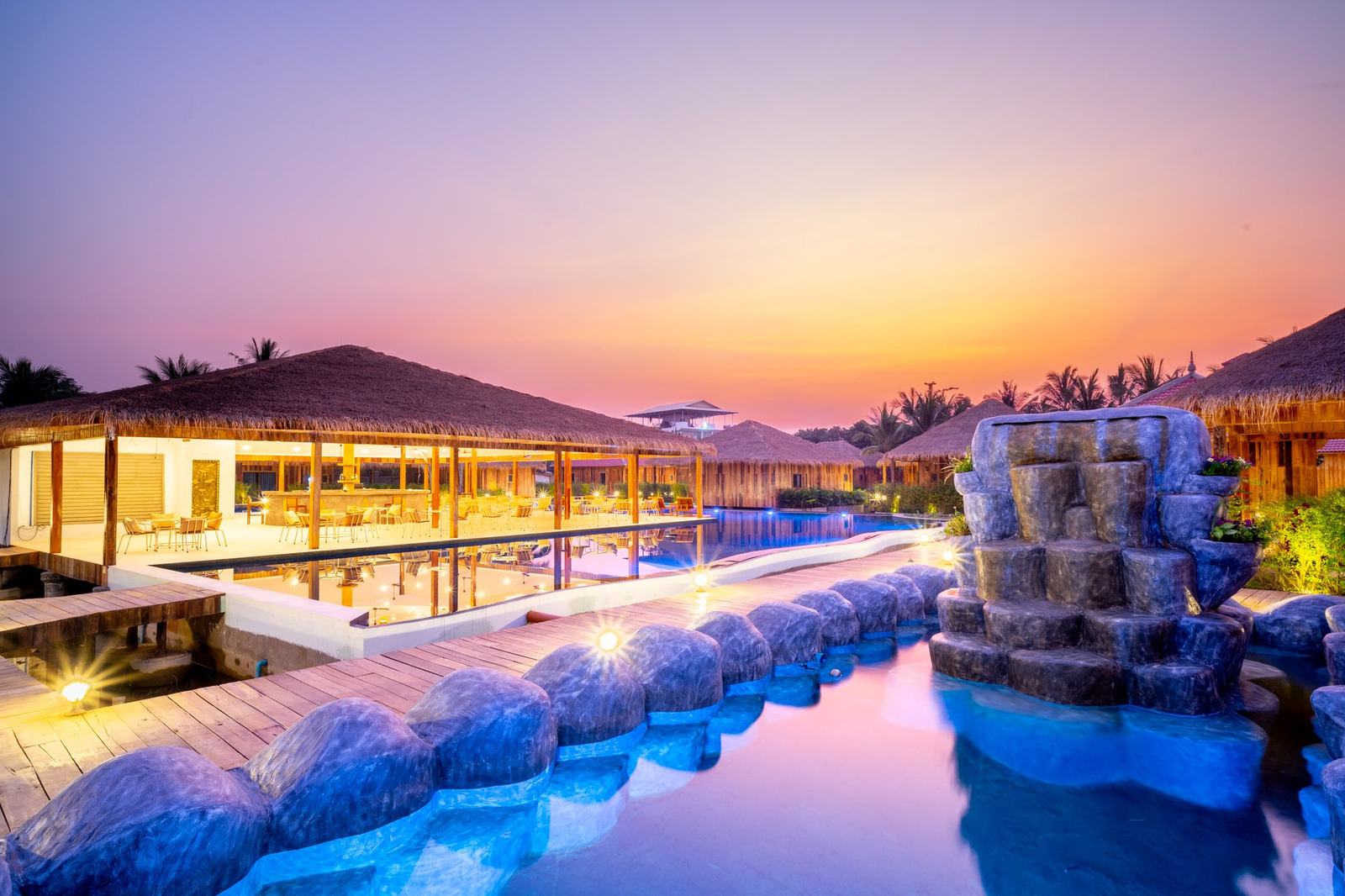 The big pool at sunset, its stone waterfall and the lit restaurant