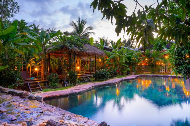 Natural stone pool in the garden at dusk, a bungalow behind