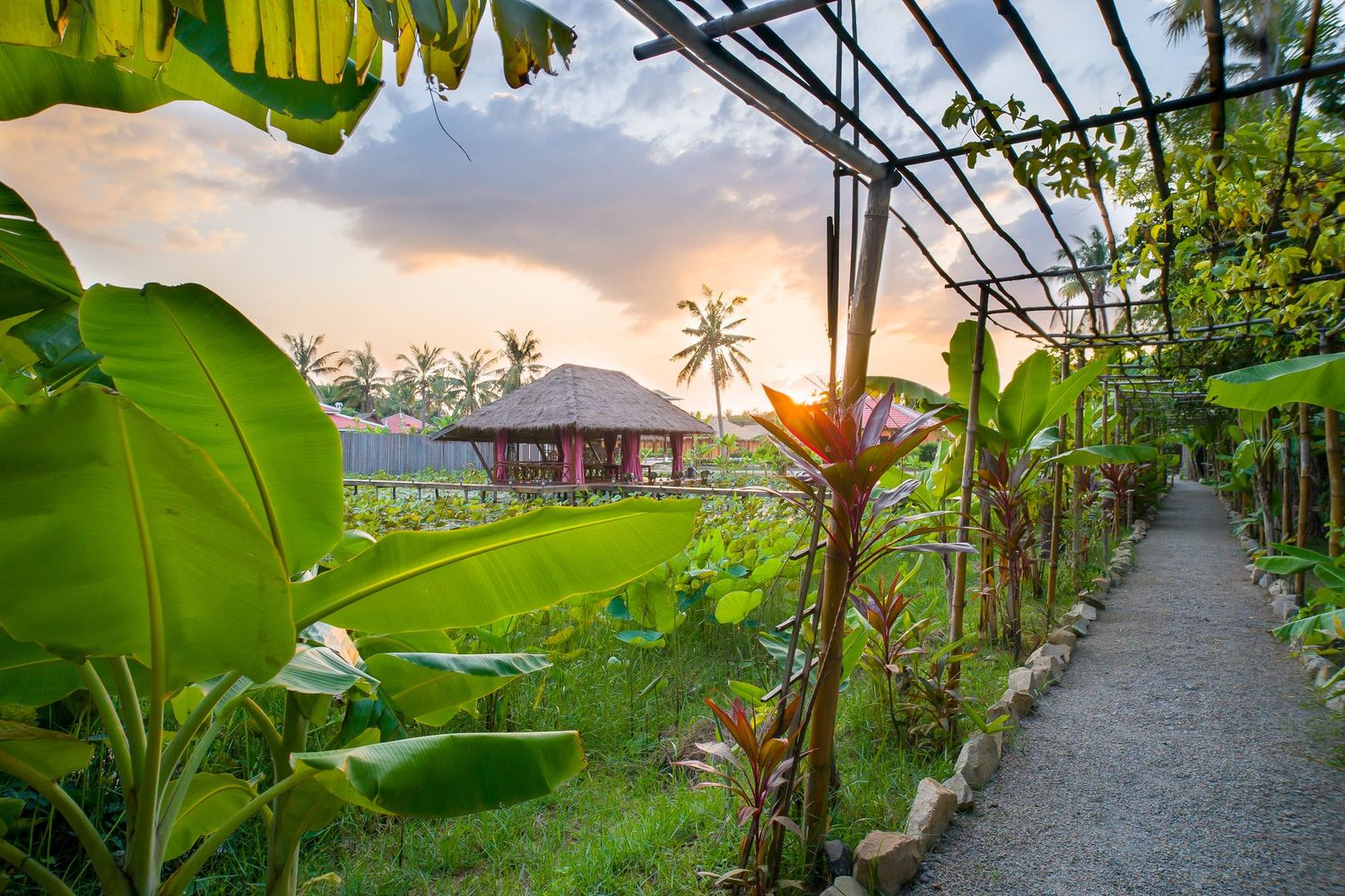 Garden path past green fields to a pavilion at sunset