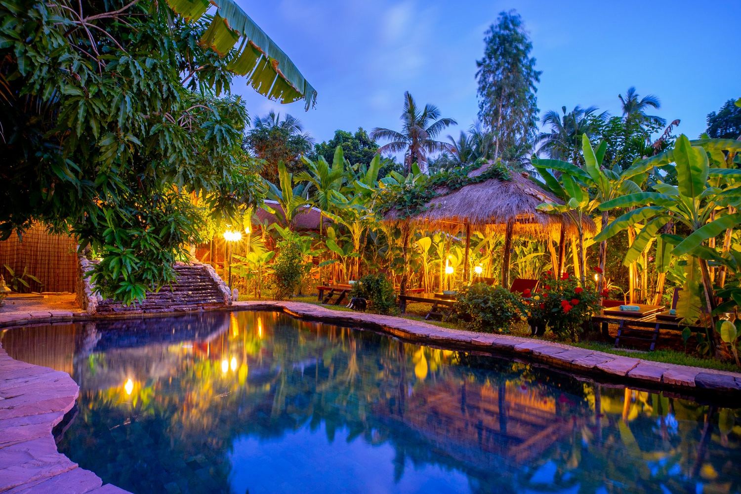 Natural stone pool among thatched salas at dusk