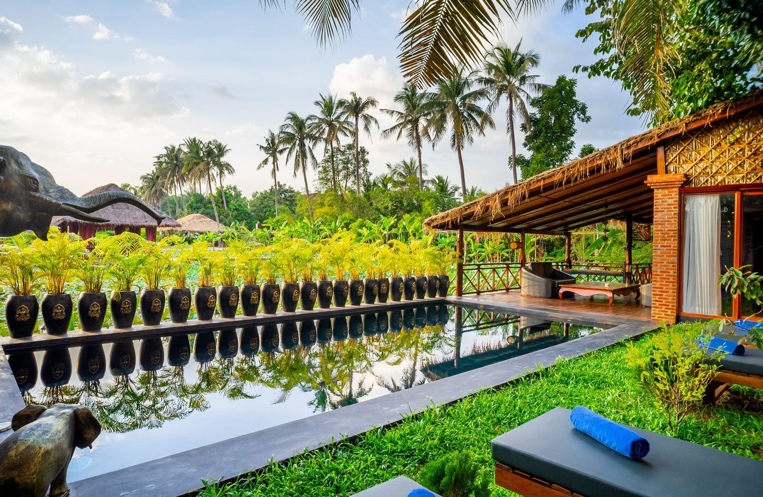 Villa Coconut's private pool lined with Khmer jars, palm trees behind